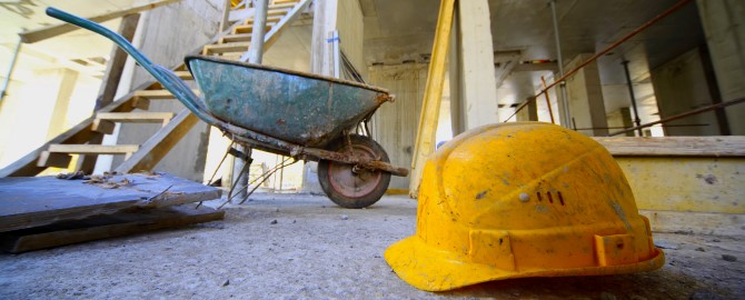 Yellow hard hats and small cart on concrete floor inside unfinished building