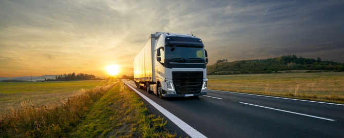 White truck arriving on the asphalt road in rural landscape at sunset